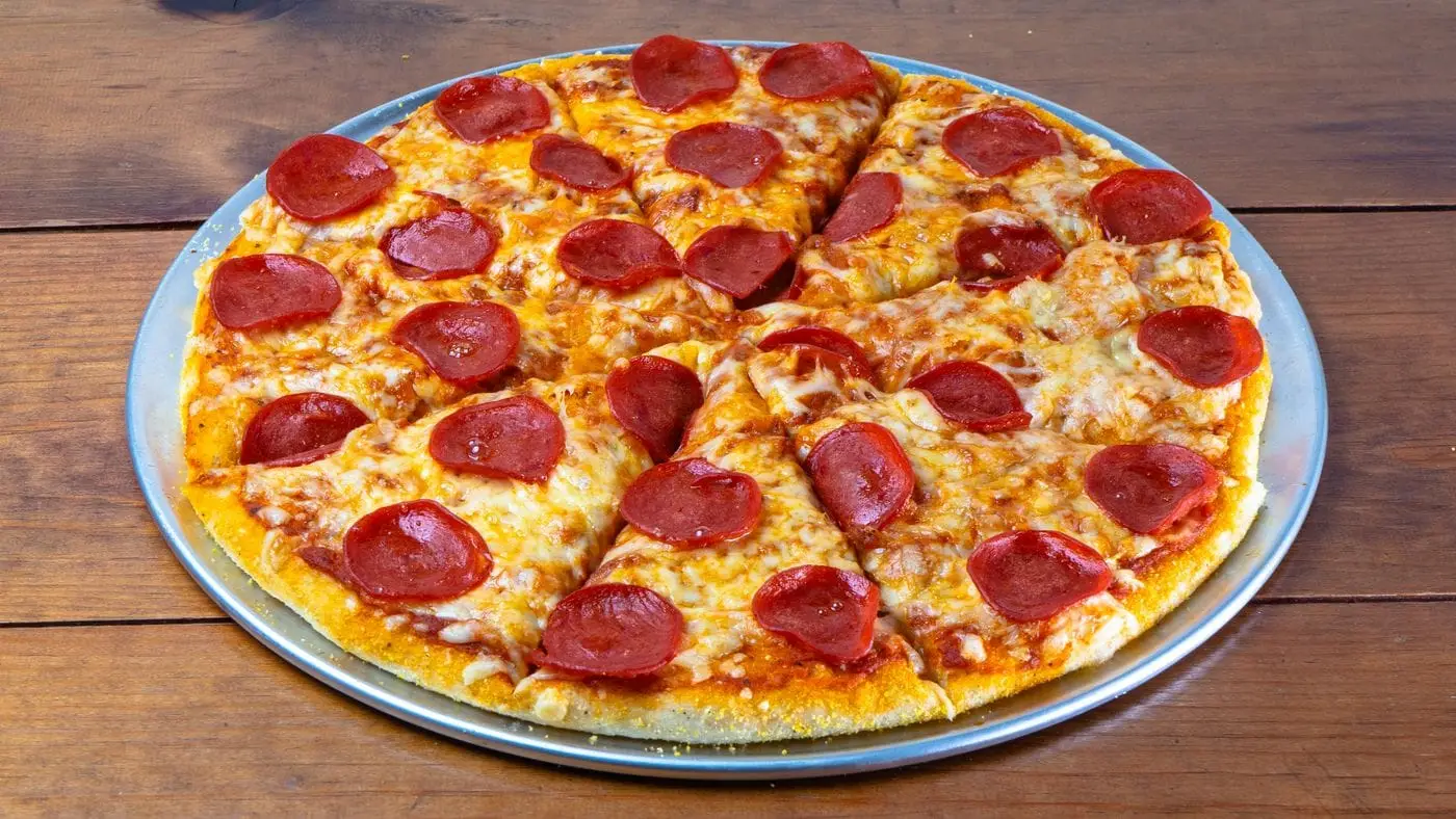 Sliced pepperoni pizza on a metal pan on a wooden table