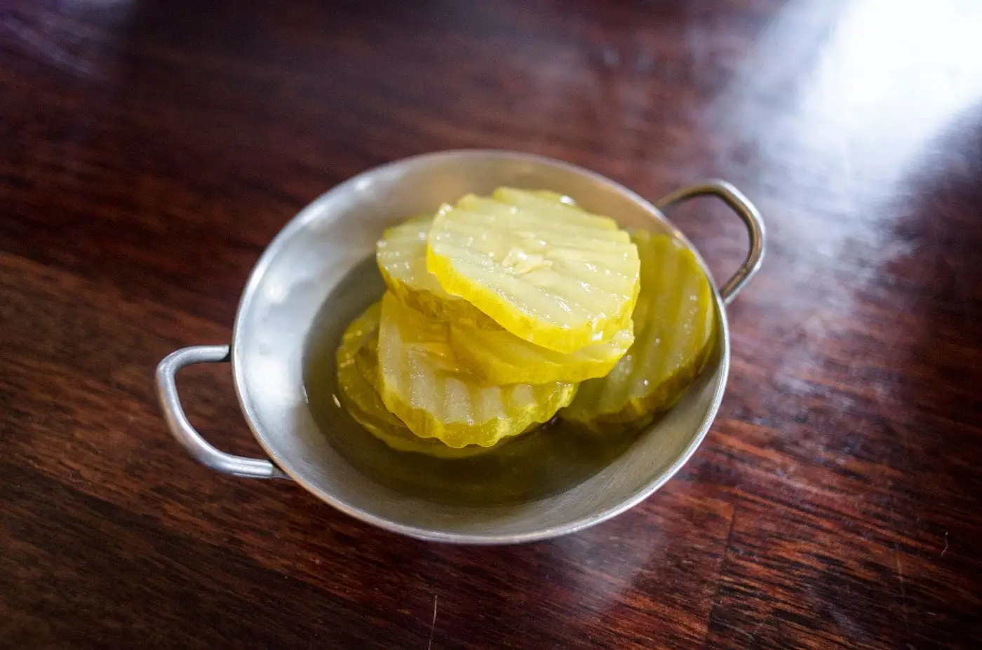 Crinkle-cut dill pickle slices in a small metal bowl on wood