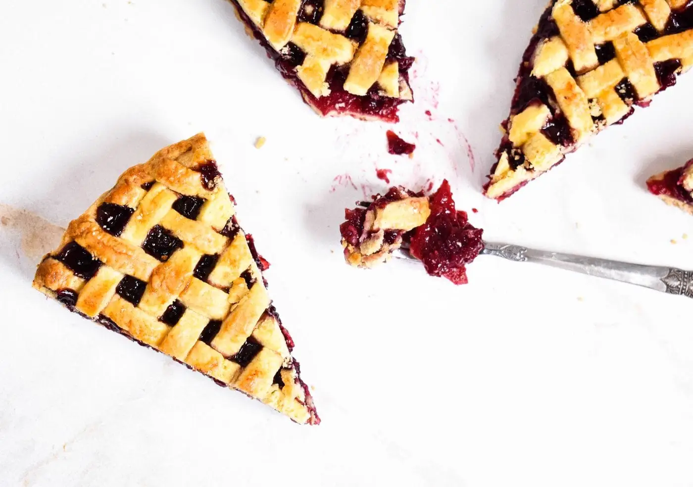 Slices of lattice-crust cherry pie on a white surface