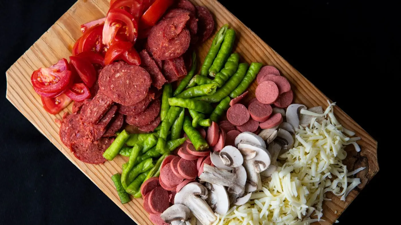 Pizza toppings of pepperoni, sausage, peppers, mushrooms, tomato and shredded cheese