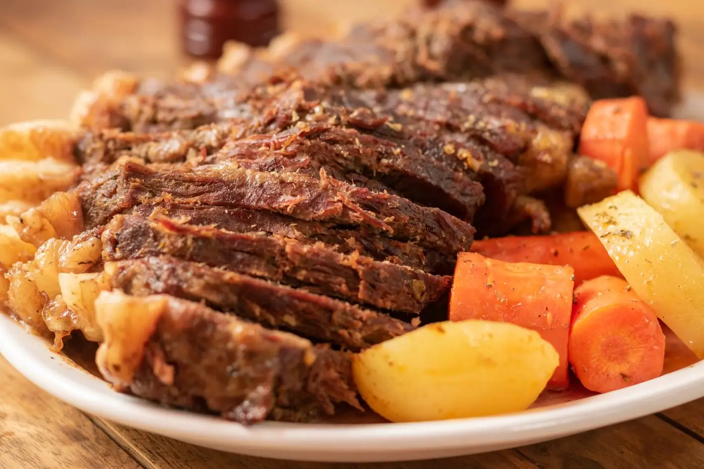 Sliced pot roast beef with carrots and potatoes on a white plate
