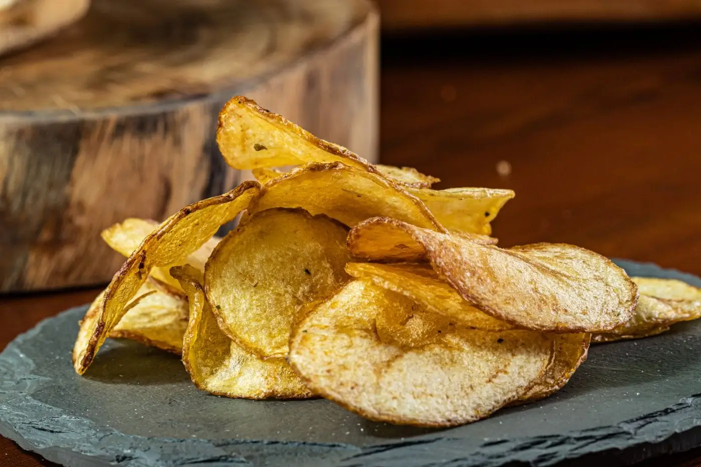 Pile of golden kettle-style potato chips on a slate plate