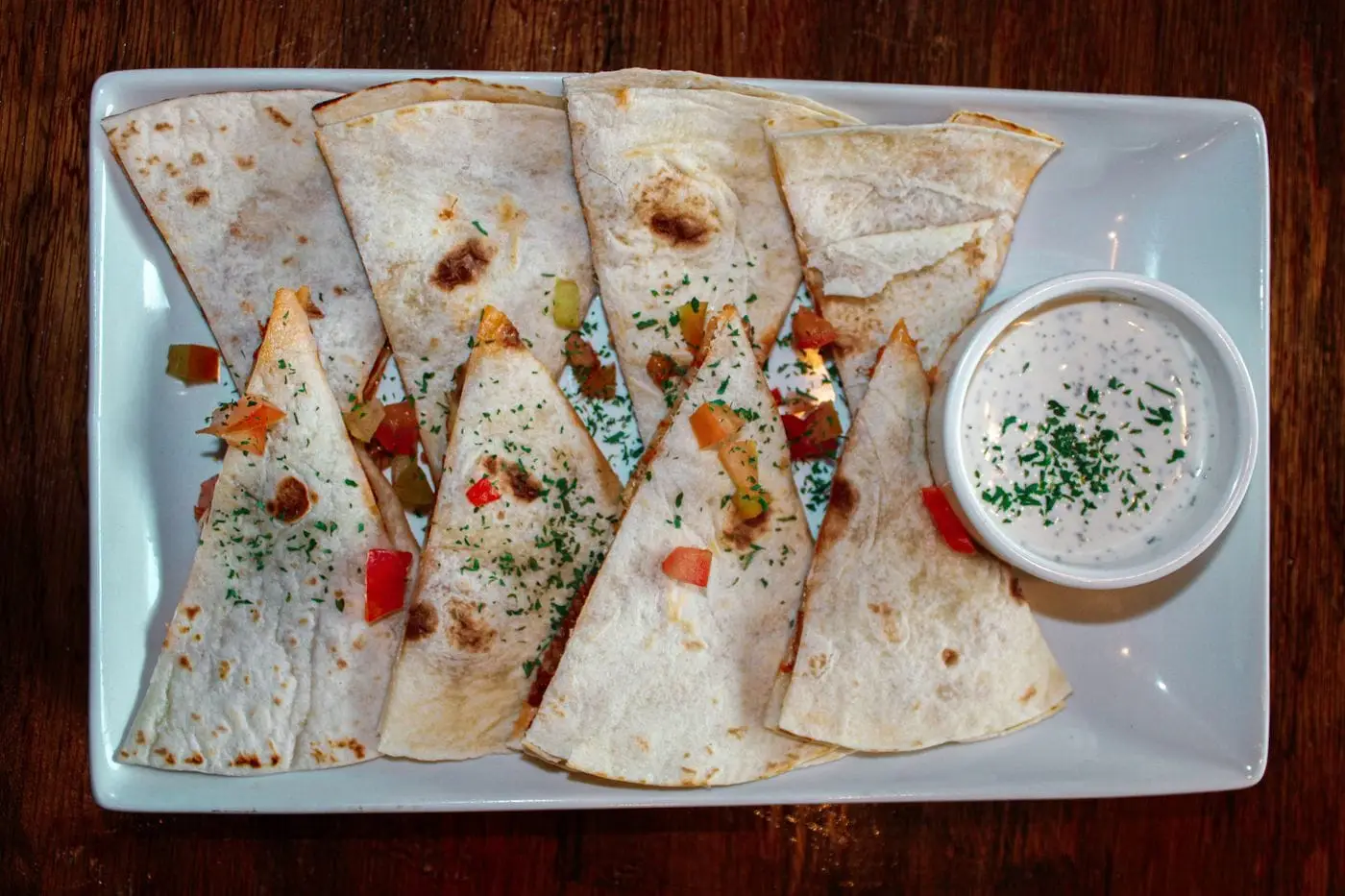 Quesadilla wedges with diced peppers and a creamy dip on a platter