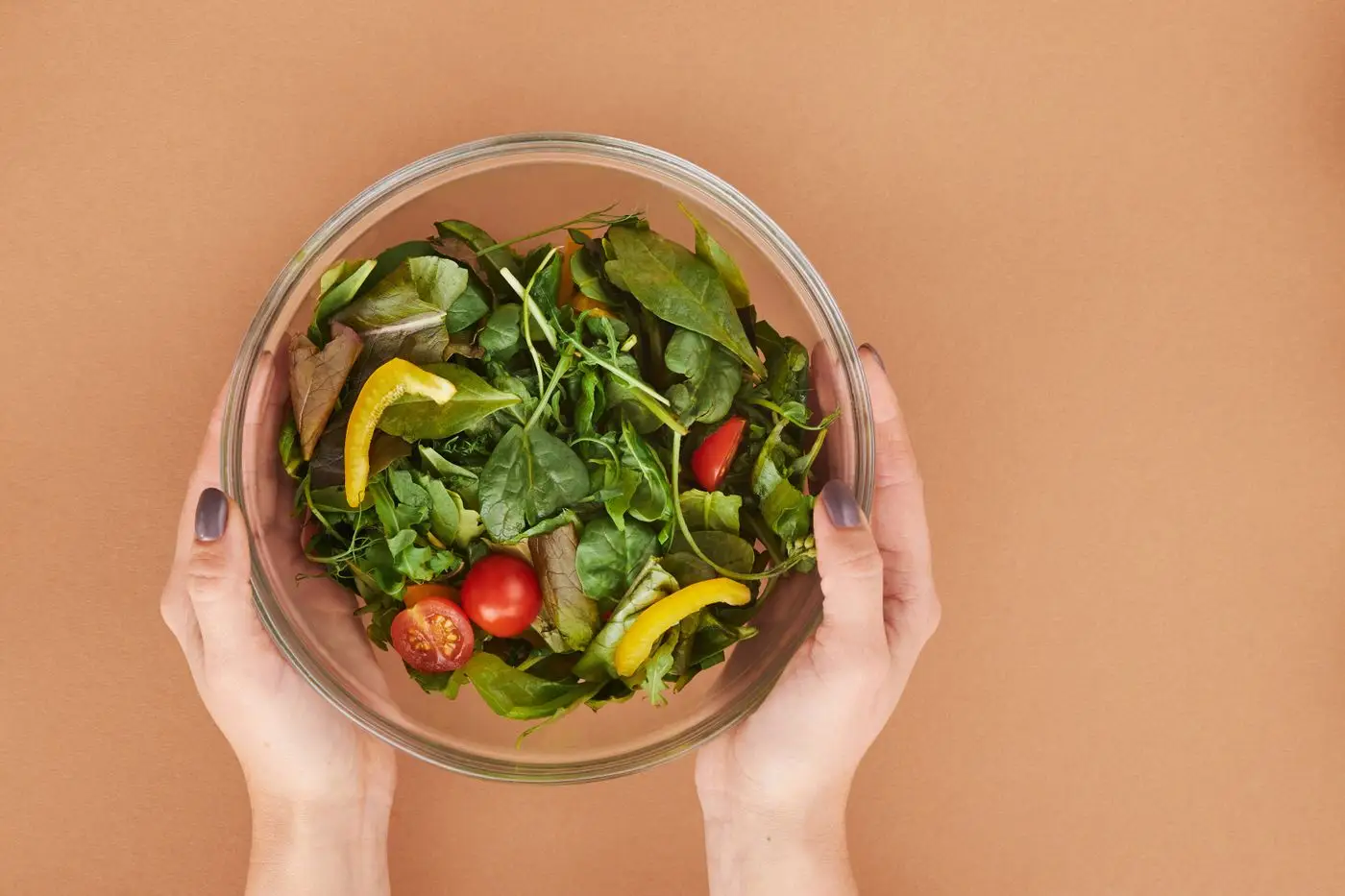 Glass bowl of mixed greens with cherry tomatoes and yellow pepper strips