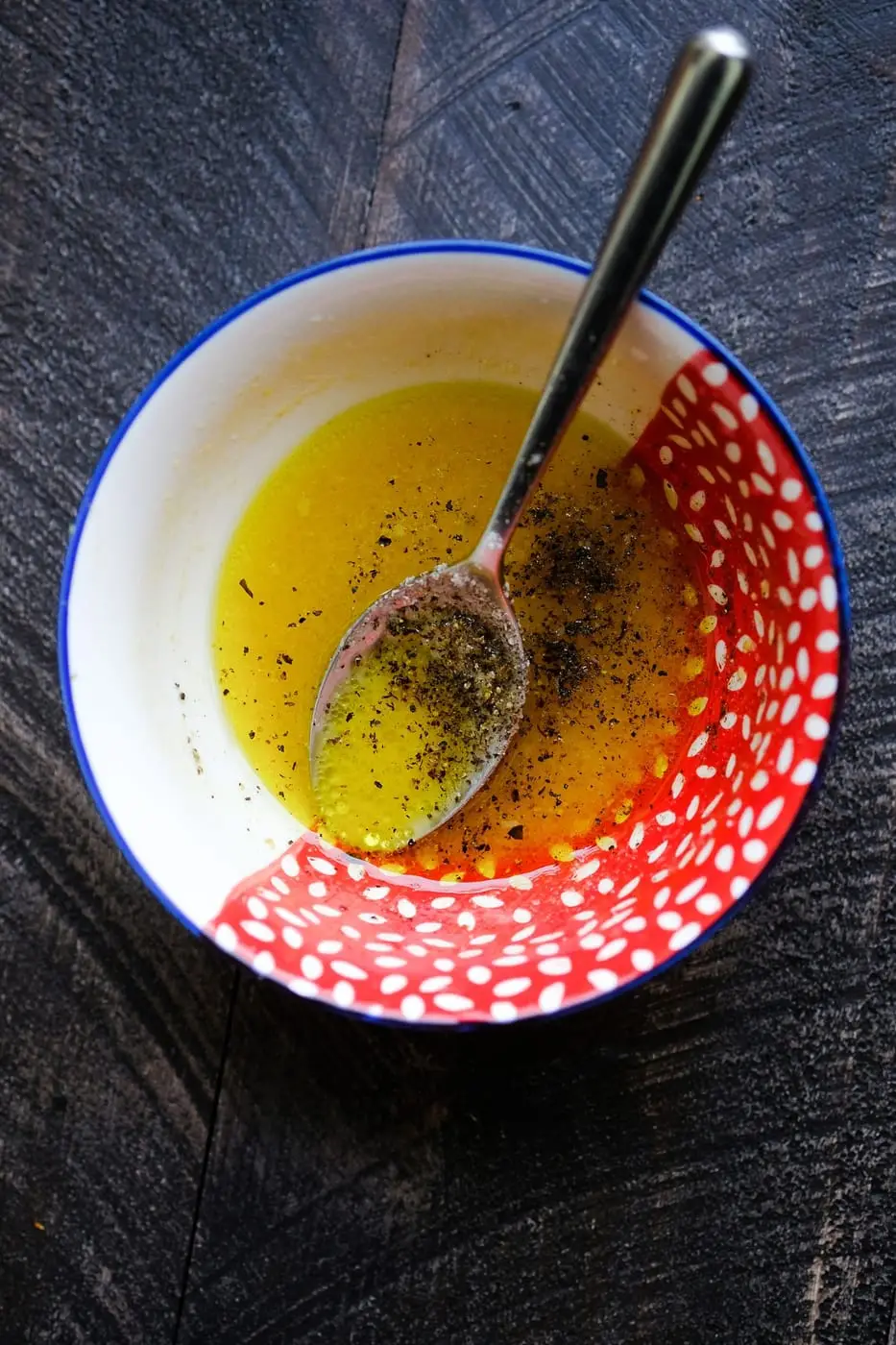 Oil and vinegar salad dressing with black pepper and a spoon in a bowl