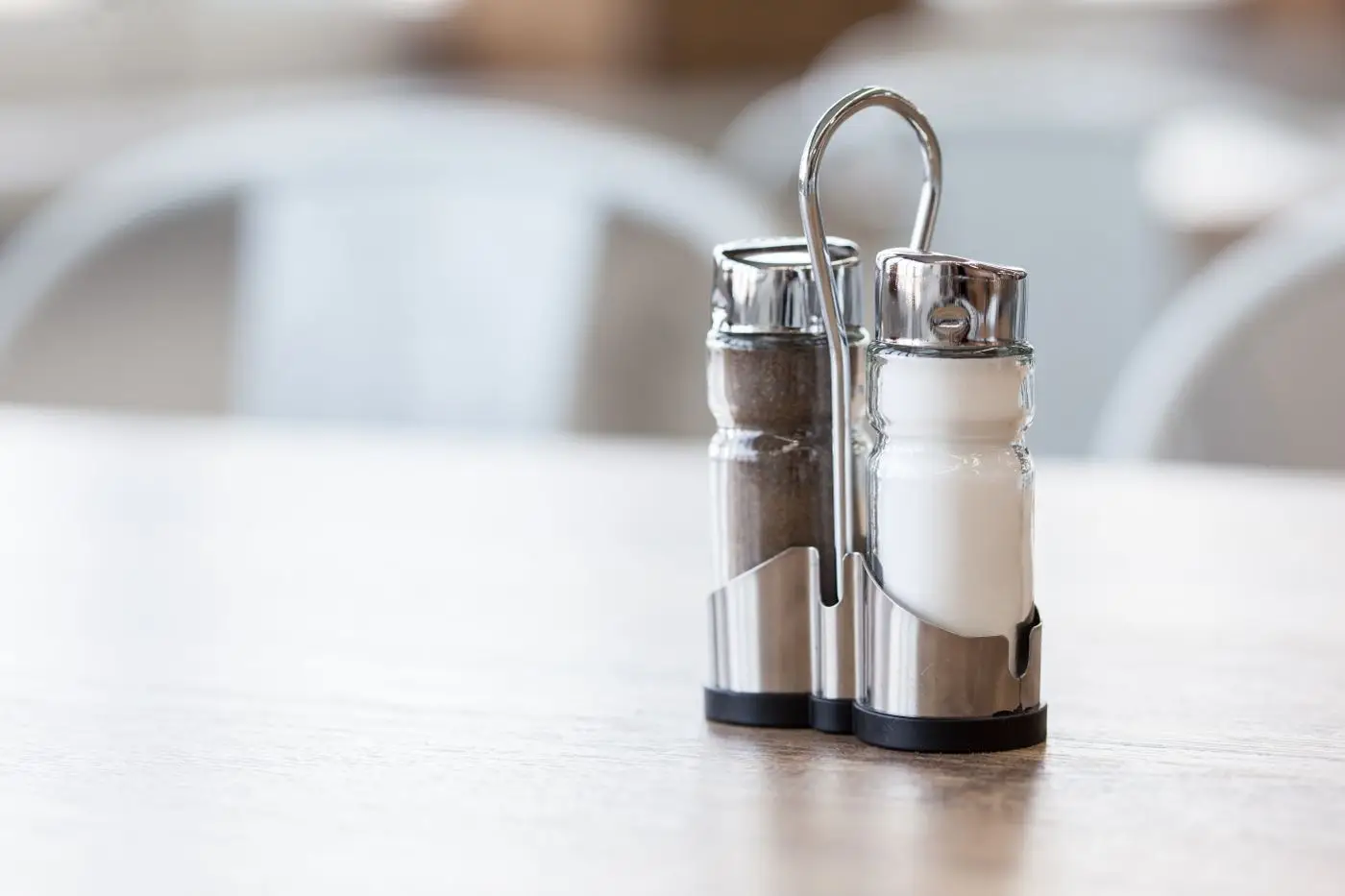 Glass salt and pepper shakers in a metal holder on a wooden table
