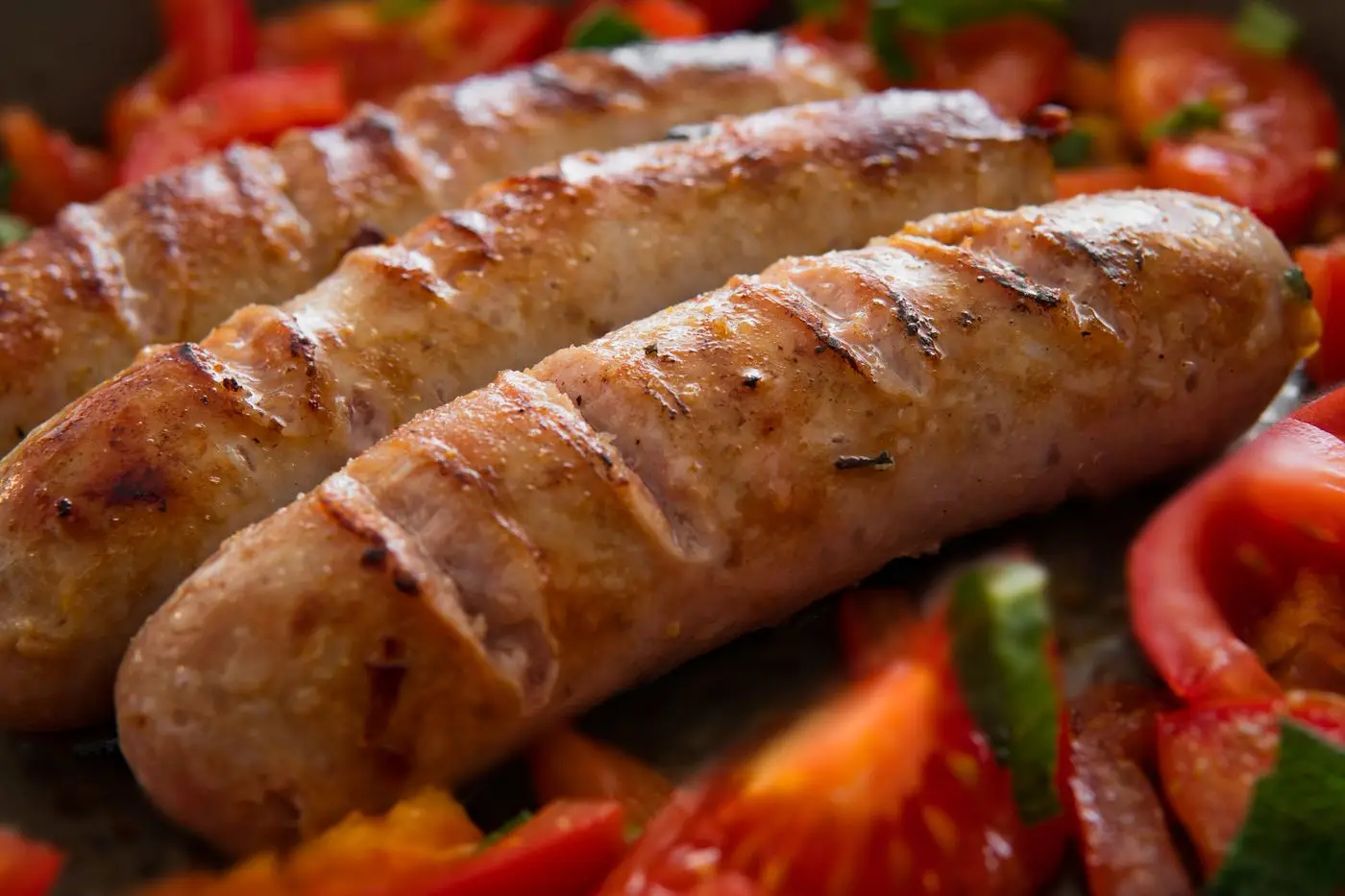Browned pork sausage links cooking in a pan with chopped tomatoes