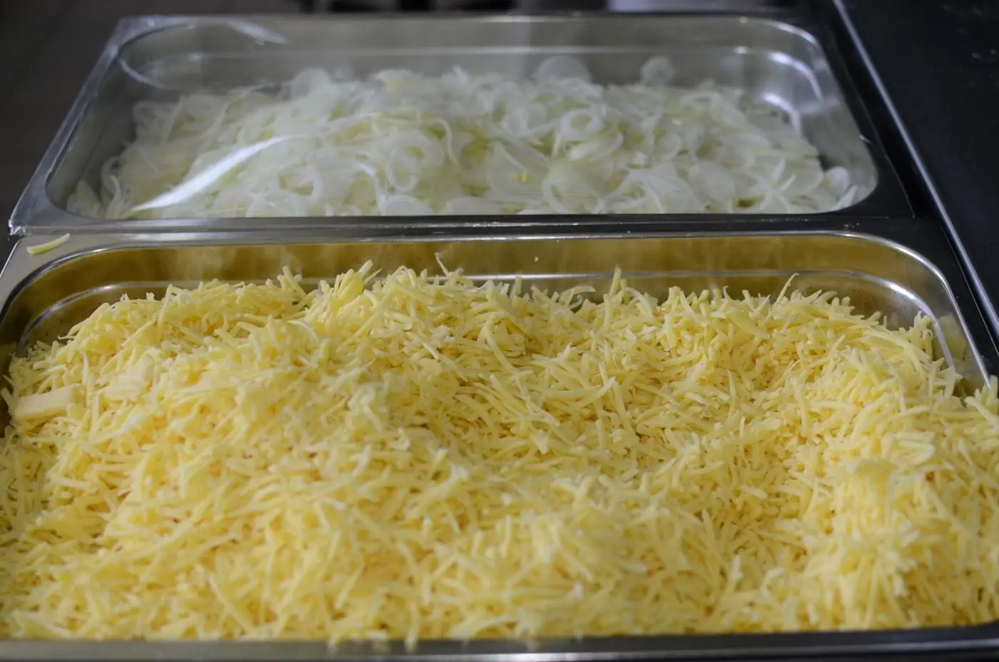 Tray of shredded yellow cheese beside sliced onions in a kitchen