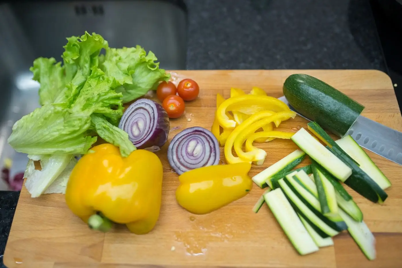 Lettuce, tomatoes, red onion, yellow peppers and zucchini sliced on a cutting board