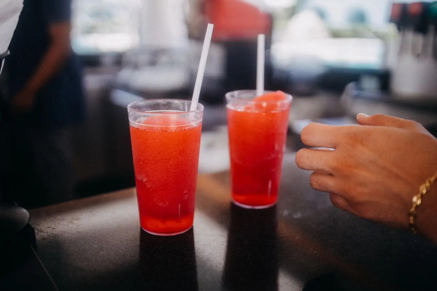Two red frozen slush drinks with straws in clear cups on a counter
