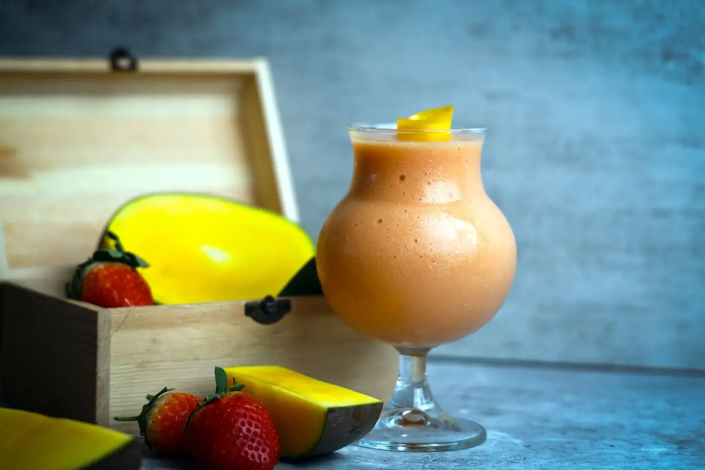 Mango and strawberry smoothie in a glass beside fresh fruit