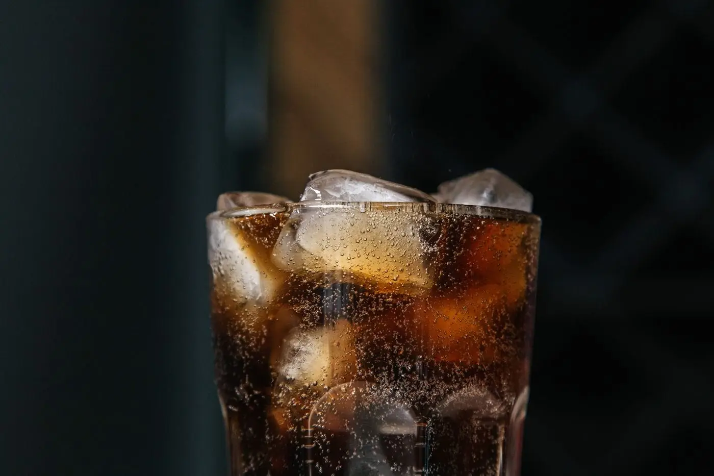 Glass of fizzy cola with ice cubes against a dark background