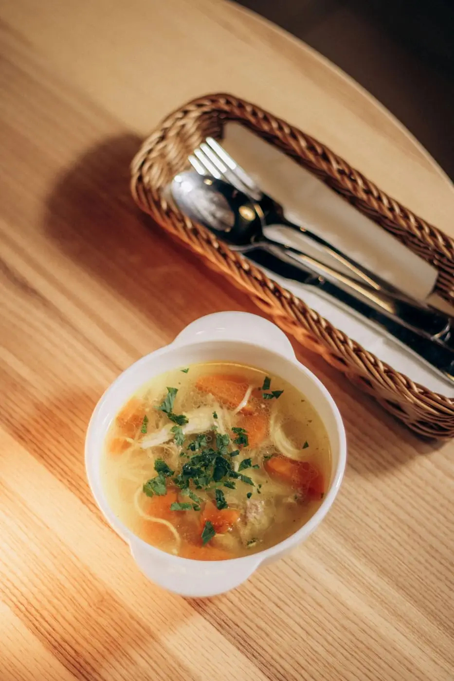 Bowl of chicken noodle soup with carrots and parsley on a wooden table