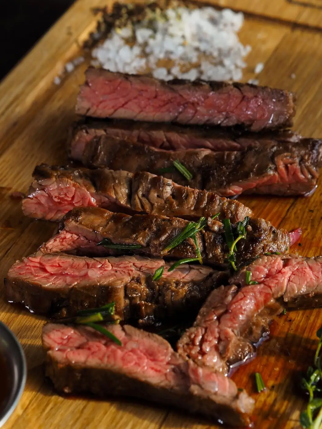Sliced medium-rare grilled steak with herbs on a wooden cutting board