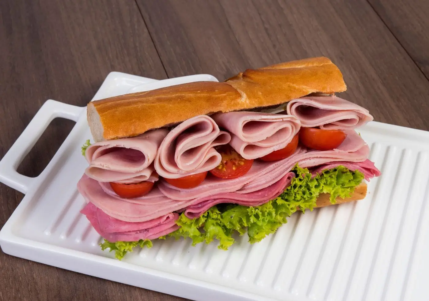 Long sub sandwich stacked with ham, salami, lettuce and cherry tomatoes