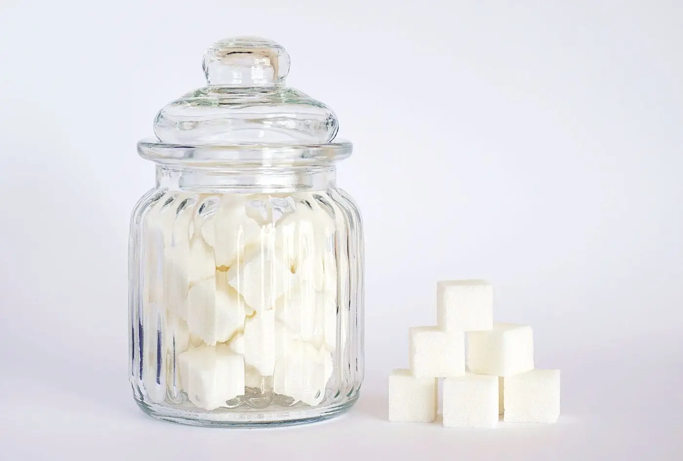 White sugar cubes in a glass jar beside a small stack of cubes