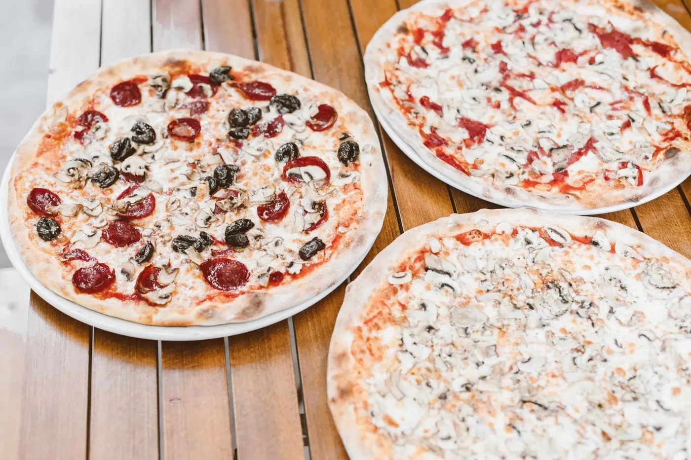Pizzas topped with pepperoni, mushrooms and black olives on a wooden table
