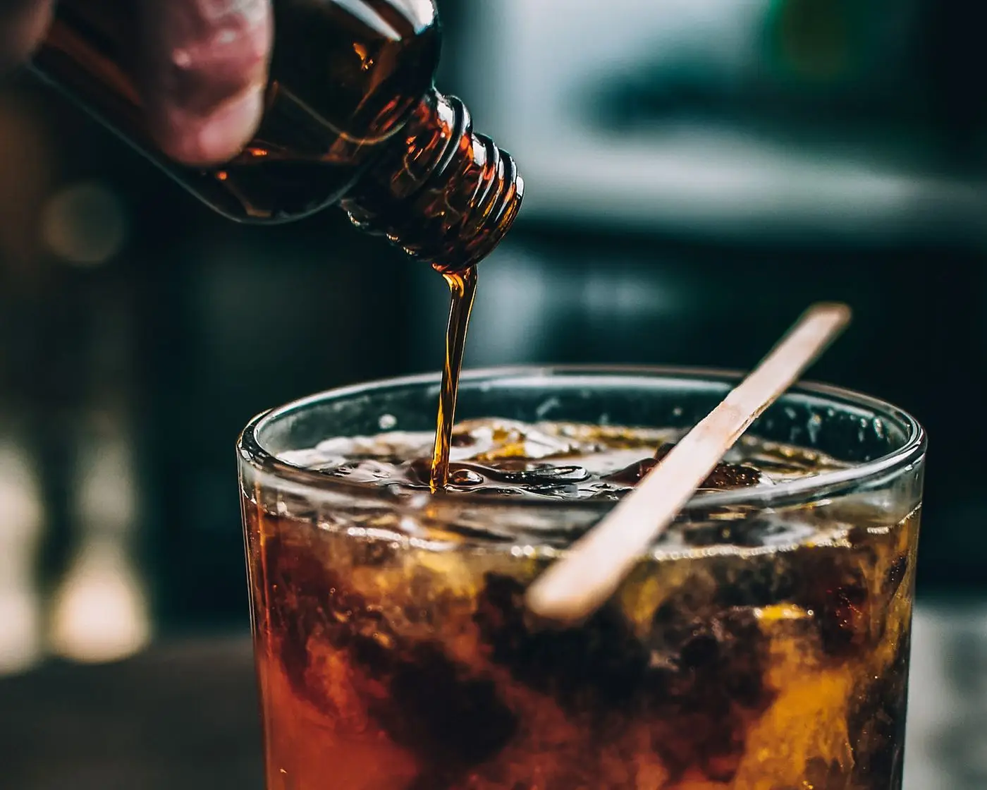 Amber syrup poured from a small bottle into an iced drink