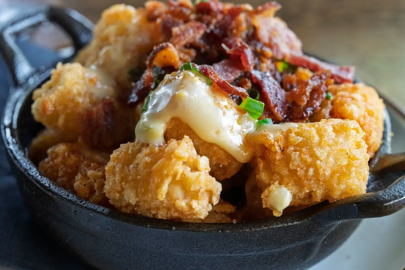 Crispy tater tots topped with melted cheese, bacon and scallions in a skillet