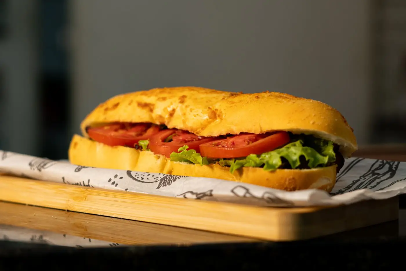 Sub roll filled with tomato slices and lettuce on a wooden board
