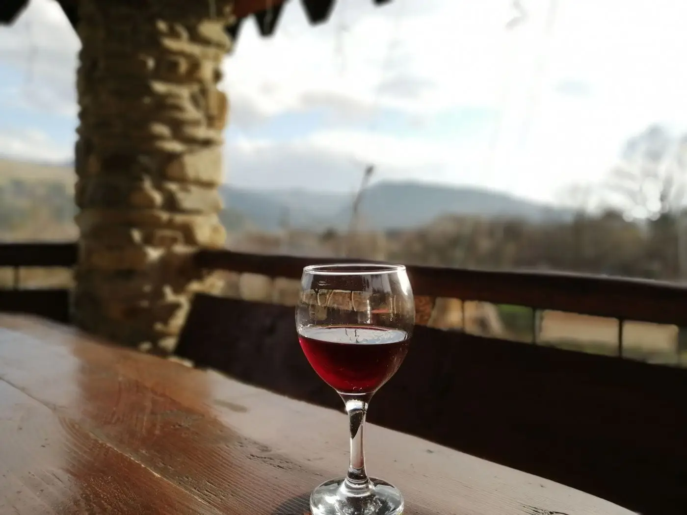 Glass of red wine on a wooden table with a blurred mountain view