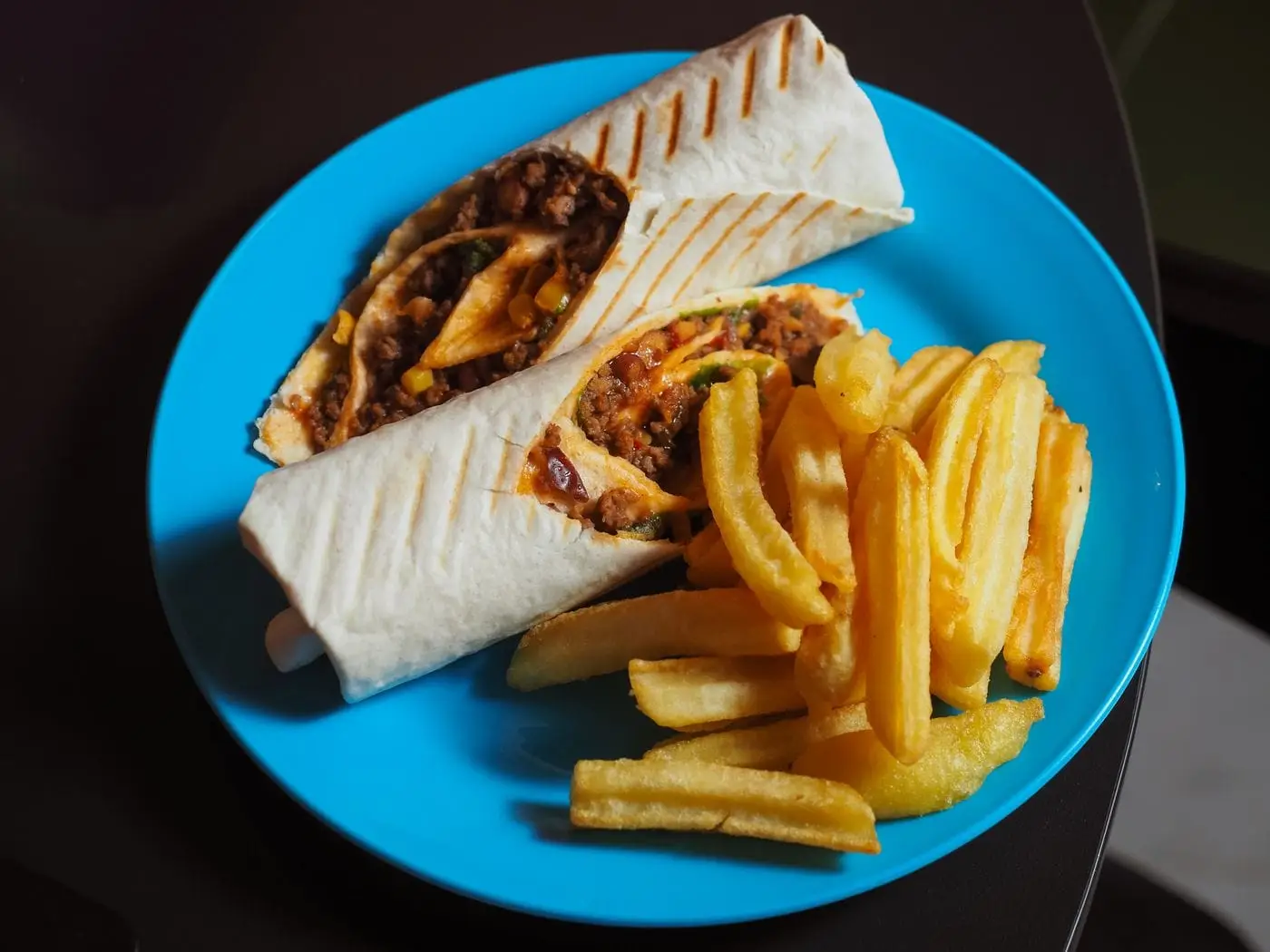 Grilled tortilla wrap cut in half with fries on a blue plate